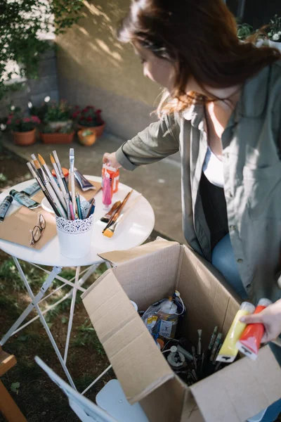 Mujer morena tomando tubos de pintura de la caja de papel — Foto de Stock