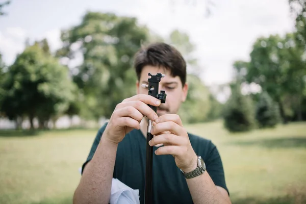 Blurred man standing behind tripod in park — Stock Photo, Image