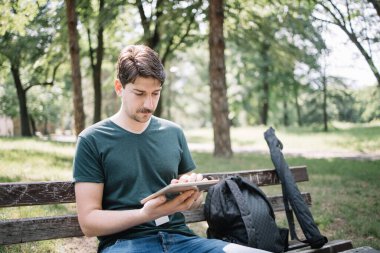 Tableti tutarken ahşap bankta oturan adamın görüntüsü