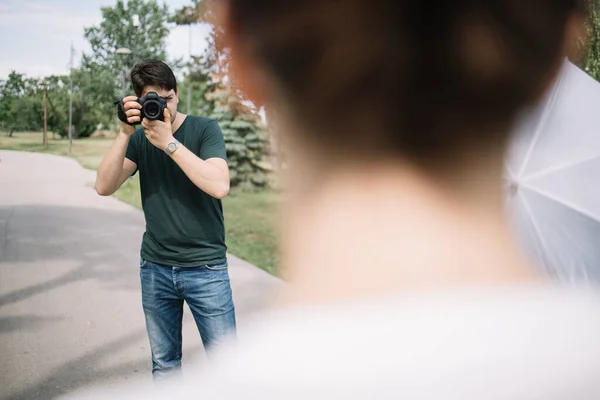 Photographer looking through camera viewfinder behind blurred woman