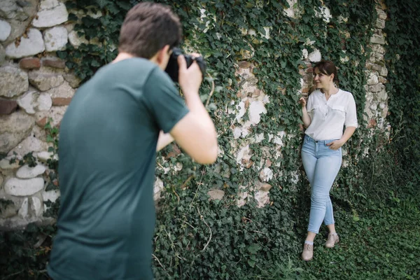 Zamazany fotograf robi sesję zdjęciową dziewczyny przed ścianą z bluszczem — Zdjęcie stockowe