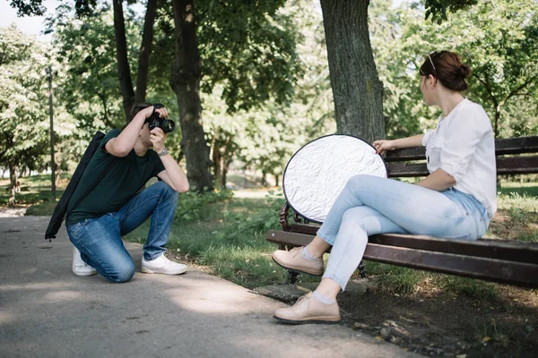 Приседающий мужчина с профессиональной фотокамерой, снимающий женскую модель — стоковое фото
