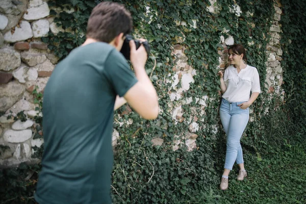 Zamazany fotograf robi sesję zdjęciową dziewczyny przed ścianą z bluszczem Zdjęcia Stockowe bez tantiem