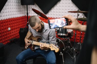 Akıllı telefonlu bulanık erkek eli gitaristin fotoğraflarını çekiyor.