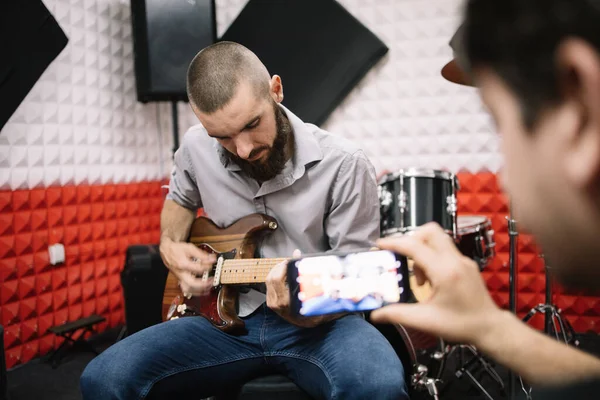 Elinde akıllı telefonuyla gitaristin fotoğraflarını çeken odak dışı adamlar.