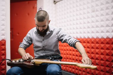 Gitarist ses geçirmez stüdyoda müzik aletini ayarlıyor.