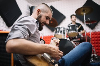 Gitarist bateristin yanında yerde oturuyor.