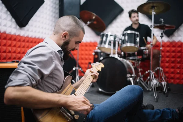 Kytarista hraje na kytaru, zatímco sedí na podlaze v hudebním studiu — Stock fotografie