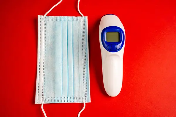 Infrared thermometer and face mask isolated on red background