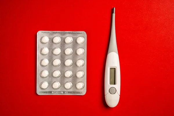 Digital thermometer and pills isolated on red background