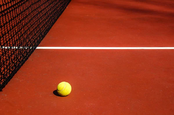 Kırmızı tenis kortunda sarı tenis topu