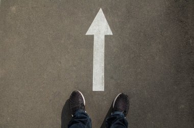 Asfalttaki beyaz bir okun önünde ayaklar