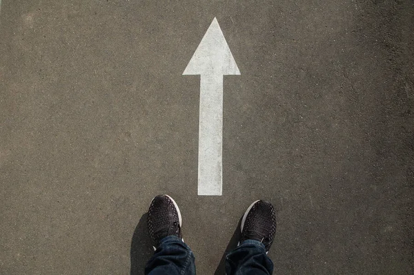Asfalttaki beyaz bir okun önünde ayaklar