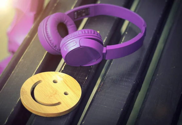 Fine music for perfect mood. Wireless headphones of purple color lie on a dark wooden bench. A wooden smile. The concept of love for music. No body — Stock Photo, Image