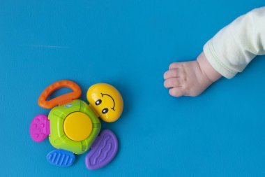 Toddler (New Born) el mavi bir arka plan üzerinde bir gülümseme ile çok renkli bir kaplumbağa oyuncak sağ uzanır. Close