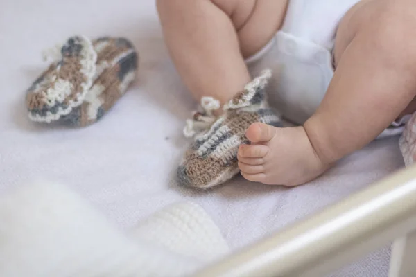 Newborn baby feet close up in wool socks on a white blanket. The baby is in the crib. One sock is removed from the foot and lies nearby, one baby foot is bare. Foot froze