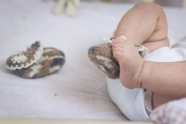 Newborn baby feet close up in wool socks on a white blanket. The baby is in the crib. One sock is removed from the foot and lies nearby, one baby foot is bare. Foot froze — Stock Photo, Image