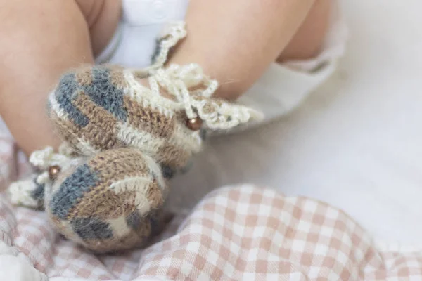 Newborn baby feet close up in wool brown knitted socks booties on a white blanket. The baby is in the crib. — Stock Photo, Image