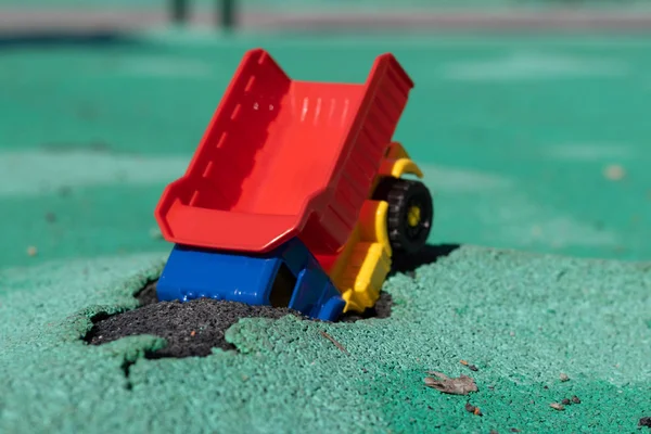 The car fell into the pit. Toy plastic truck with a red body had an accident. Hole on Asphalt Coating. Accident has occurred — Stock Photo, Image