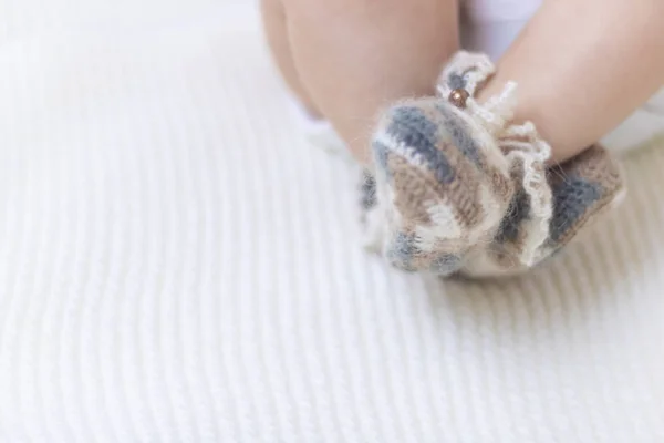 Новорожденные детские ноги закрываются в шерстяных коричневых вязаных носках ботинках на белом одеяле. Ребенок в кроватке — стоковое фото