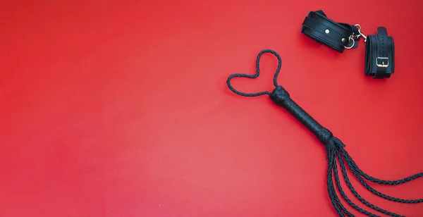 Accessories for bdsm on a red leather background. Lash in the shape of a heart and leather handcuffs. Valentines Day. Erotic shop. Copy space — Stock Photo, Image