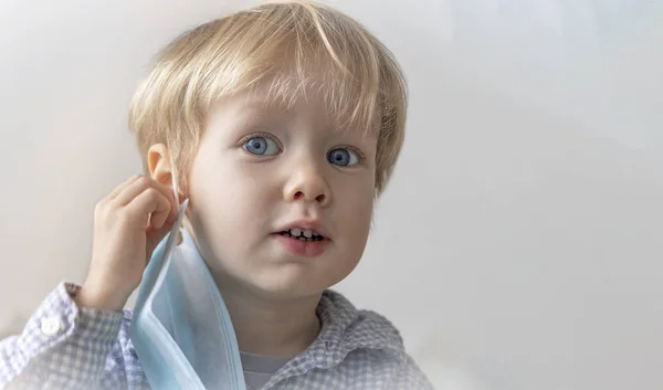 Europeanan Caucasian boy child kid toddler took off his medical mask on a gray background. Baby is healthy. Concept of recovery, health, medicine, the end of a epidemic. Copyspace, Mockup, free spase — Stock Photo, Image