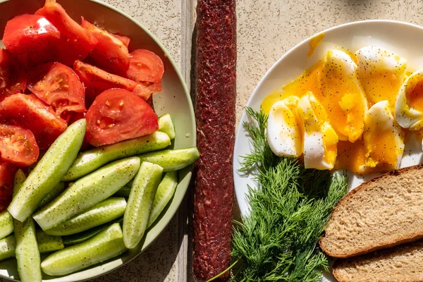 Sliced egg with soft yolk, vegetables, cucumbers, tomatoes and dill with a piece of brown bread. Healthy and tasty breakfast or dinner. Homemade country house food
