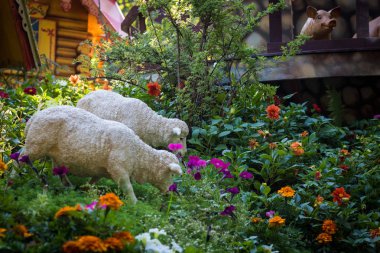 İki beyaz koyunun figürleri. Hayvanlar çiçek çayırında otlarlar. Harika bir bahçe, tarım, çevre dostu.