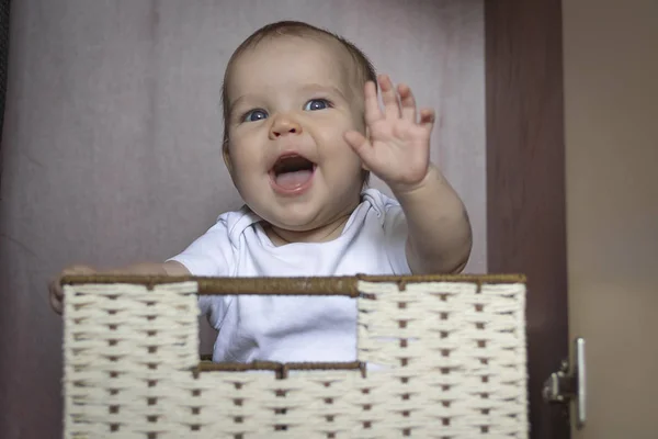 Europeu caucasiano Joyful criança, criança, menina, menino sorrindo e senta-se em caixa na cesta de vime No armário para armazenamento em fundo escuro. Conceito de armazenamento no berçário, ajuda aos pais, infância, educação — Fotografia de Stock