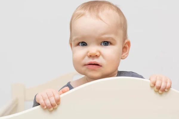 Portrait european caucasian happy smiling baby toddler with blue eyes on a white background looking at the camera holding on to the bed. Age - 10 months - 1 year. — Stock Photo, Image