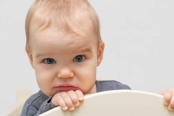 Retrato de uma criança europeia caucasiana bebê triste, enruga a testa, olha para a câmera, se agarra à cama. Num fundo branco. Idade - 10 meses - 1 ano . — Fotografia de Stock