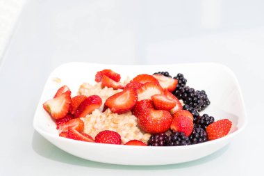 Beyaz bir arka plan üzerinde çilek ve böğürtlen ile yulaf ezmesi lapası beyaz bir tabak kase yakın çekim. Yan görünüm. Sağlıklı vejetaryen yemek ve lezzetli kahvaltı kavramı. Diy hasat