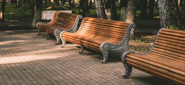 Parkta üç retro eski banklar hiçbir insan vardır, günbatımı ışık gölgeler ve aşırı pozlama oluşturur, biraz sonbahar yaprakları. Yatay fotoğrafçılık