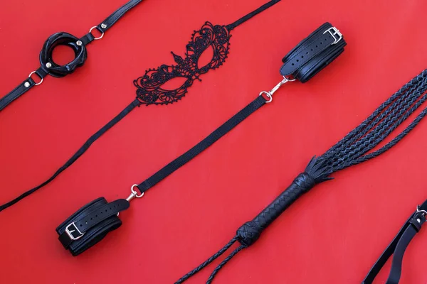 Set for bdsm handcuffs, whip, mask, on a red leather background. Top view flat lay, diagonal layout — Stock Photo, Image