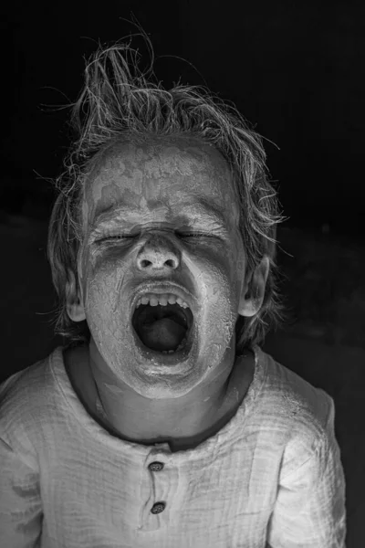 Niño asustadizo con una arcilla blanca untada o cara de maquillaje blanco y negro monocromo — Foto de Stock