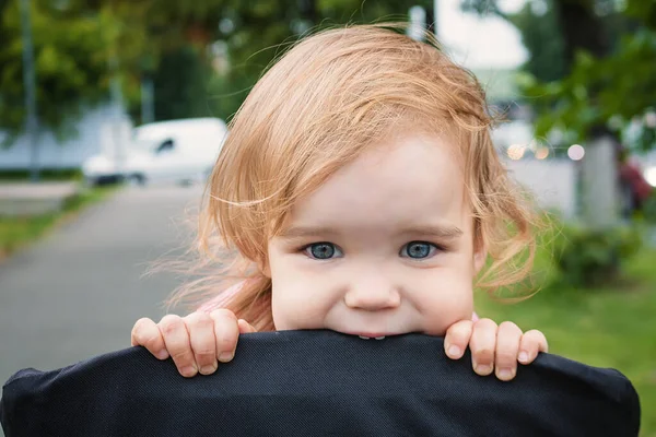 Retrato de uma menina pequena criança engraçada loira com olhos azuis sentados em um carrinho de bebê no verão para verdes. Uma garota alegre engraçado virou-se em um carrinho de criança por um ano e morde-lo — Fotografia de Stock