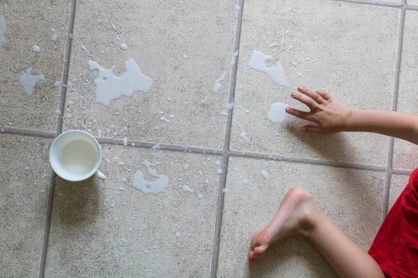 Childs bosé nohy stojící v kaluži rozlitého mléka na podlaze s bílým pohárem — Stock fotografie