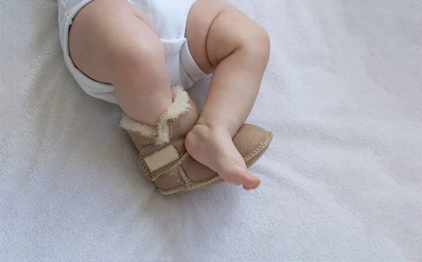 Ноги новорожденного малыша крупным планом на кровати. На одной ноге ботинки из кожи и меха. Вторая нога босиком. Нога замерзла. Обрезанные вертикально и горизонтально — стоковое фото
