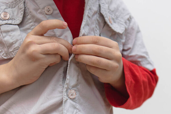 Childhood independence concept ,little boy buttoning on shirt, fastening his buttons , isolated on white gray background. The child puts on his own clothes