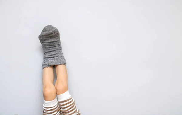 Childrens feet in one woolen sock. The legs are frozen, my mothers concern is to dress the child. Heating, cooling, autumn concept on gray background copy space. Mother tied son with her care