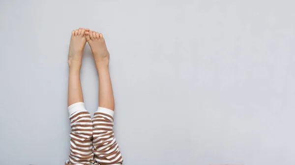 Los pies de los niños se levantan descalzos. Un niño sin calcetines con los pies desnudos en pijama a rayas. Concepto de calefacción para niños, habitación cálida y maternidad. espacio de copia — Foto de Stock