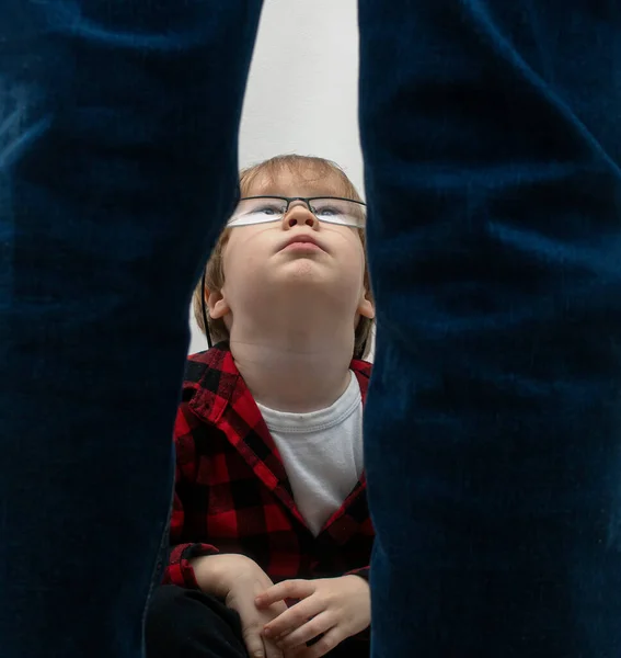 Um menino com óculos está sentado e olhando para o homem de pé em desânimo. Violência doméstica, rapto e conceito de abuso infantil — Fotografia de Stock