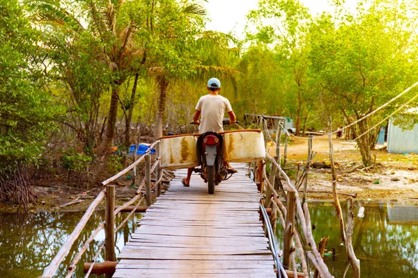 Vietnamese on a bike with baskets in a tropical park passes over the bridge