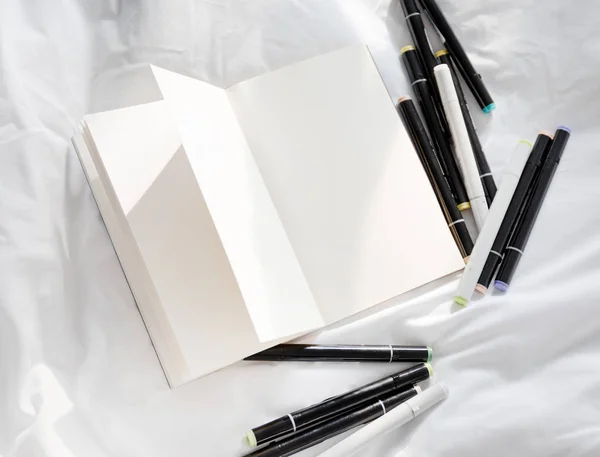 Blank åben dagbog på en hvid seng med bunke kuglepenne - Stock-foto