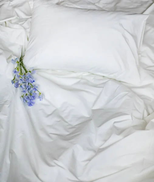 Flowers on the messy bed, white bedding items and blue flowers bouqet — Stock Photo, Image