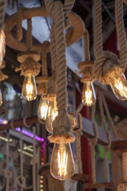 Dükkanın önünde çekilmiş. Halat, kahverengi ip ve sarı ışıkta asılı lambalar