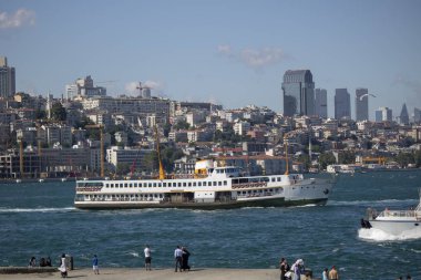 İstanbul, Türkiye - 27 Haziran-2019: Sarayburnu sahilinden alınan deniz manzarası, balıkçılık ve yürüyen insanlar. Arka planda deniz ve şehir silueti üzerinde geleneksel buharlı gemi.