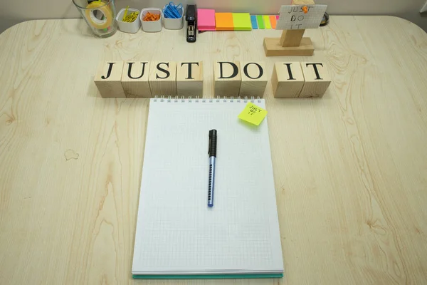 There is a notepad checker and pencil on the table. On the right, it says, Just do it, with a wooden cube. Studio was photographed.