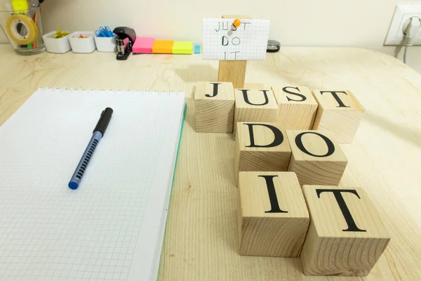 There is a notepad checker and pencil on the table. On the right, it says, Just do it, with a wooden cube. Studio was photographed.