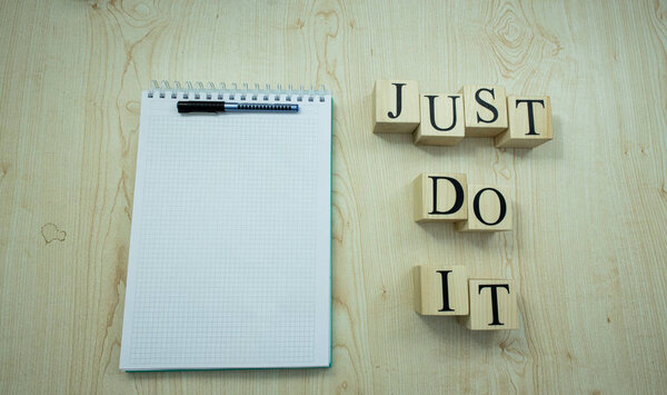 На столе есть блокнот и карандаш. Справа написано: Просто сделай это, с деревянным кубом. Студия была сфотографирована
.